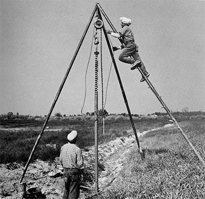 Auger-bit of the McCullough drill being pulled out with its sample by a chain-hoist and tripod.