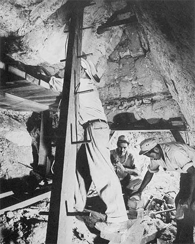 Three men erecting beams to support the roof of a vault.