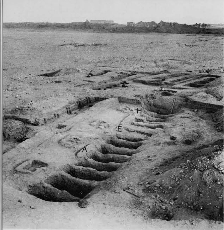13:483 and 13:484 partially excavated. Traces of the denuded mud-brick coping of group 13:484 can be seen west of shafts A and E to H. In the center background is the temple of <a target=