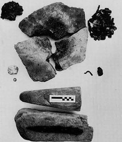 Metalworking at Pithekoussai. Clockwise from the upper left: Sponge-like lump of iron "bloom" ; large, course sherds from Structure III floor burned by a bellows-fed fire until vitrified at center; fragments of iron and slag associated with sherd hearth; small piece of a  bronze ignot (?); miscast bronze fibula; whetstones from Structure IV with an iron knife on the lower one; bronze and lead disc-shaped weight; lump of lead. 