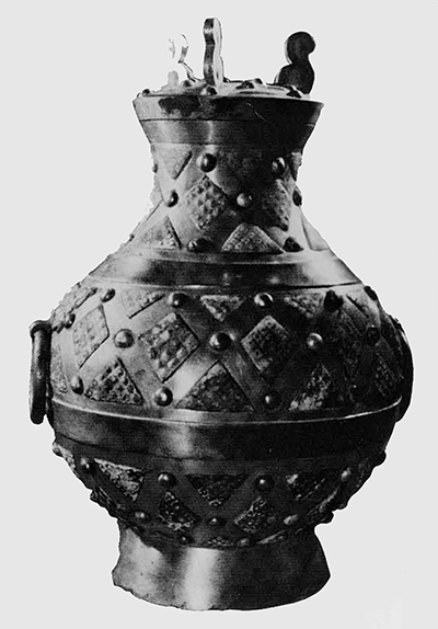 A rare type of gilded bronze wine vessels (hu) found in the king's tomb. It is partitioned by silver bands into horizontal zones, each filled with squares and triangles inset with a greenish stone and divided by bands with embossed nail-heads. According to an inscription "Ch'ang-lo ssū-kuan chung," this was a vessel containing a chung, (a measurement equal to 4 tou pecks) in the Ch'ang-lo (palace of Eternal Joy) for which the Office of Provision was responsible. Date: First part on 2nd century B.C. Kaogu 1972. No.1. Pl. V, 1. 