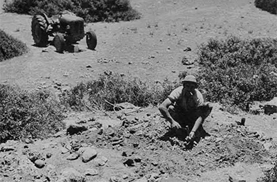 A man crouched, picking through rocks and fossils on the ground.