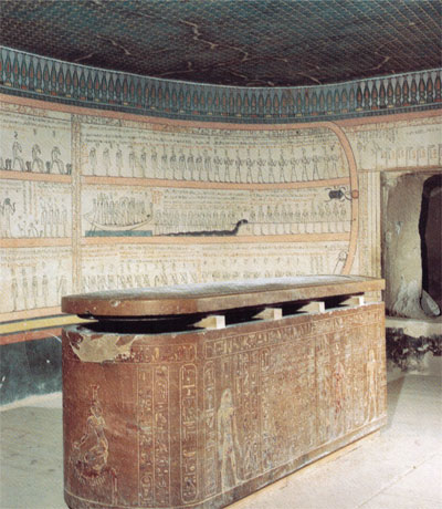 View of a tomb with a massive stone sarcophagus next to a curved tomb wall.