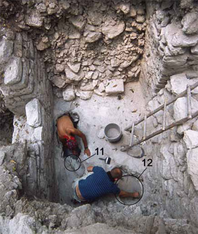 View looking down into an excavated pit, two men carefully digging around a burial.