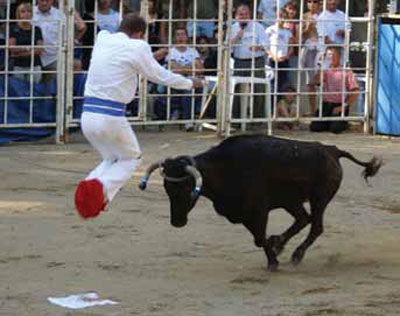 A person wearing all white except for red shoes, mid leap as a bull rushes them.