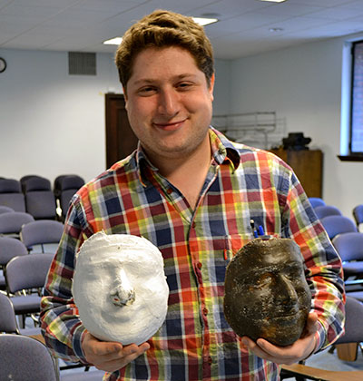 A person holding a plaster mold and a wax mask made from the mold side by side.