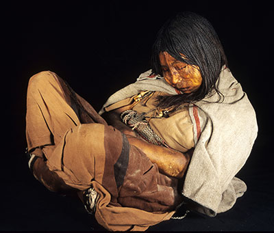 The preserved body of a child, seated with legs crossed, head bowed to chest.