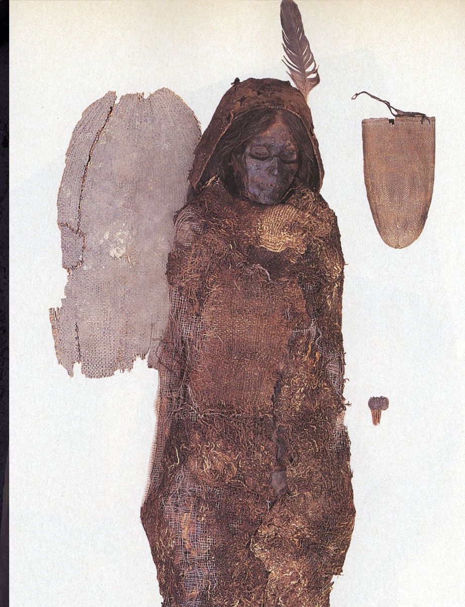 A mummy surrounded by burial objects, wrapped in a thick cloak.