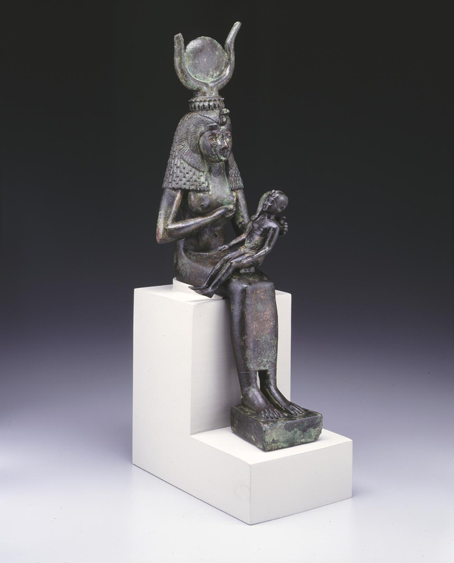 Bronze statuette of Isis nursing the infant Horus. Isis wears a long, tight-fitting dress and a vulture headdress with uraeus, horns and sun disk.