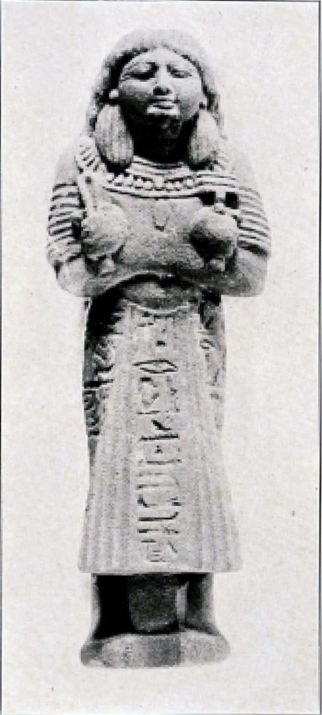 Black and white photo of sandstone statuette, person in a long gown, arms crossed close to chest with object in each hand. Hieroglyph inscription down front.