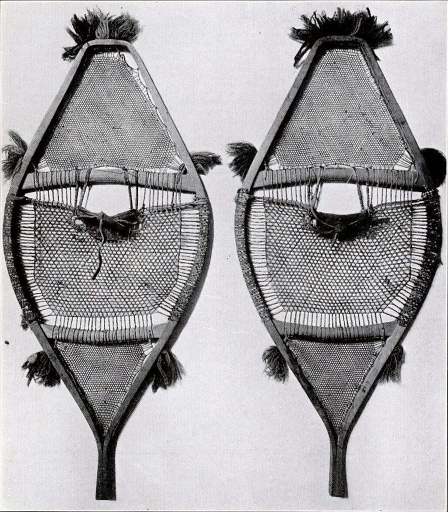 A pair of snow shoes broad in the foot and toe and arrow at the back with tufts of fabric on the outside