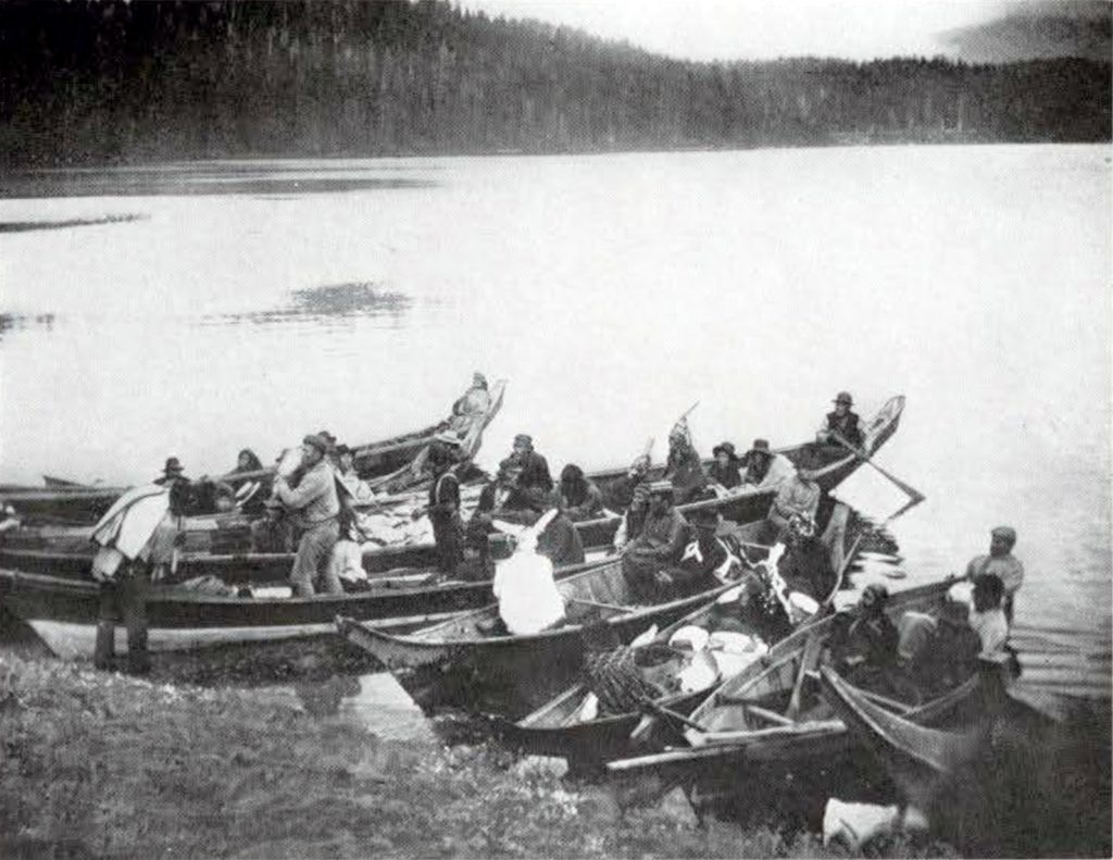 A large group of people in six canoes, dismounting onto the shore