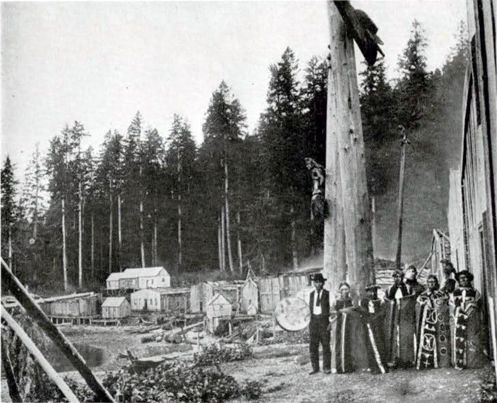 A group of people standing next to tall, bare trees, with a village in the background