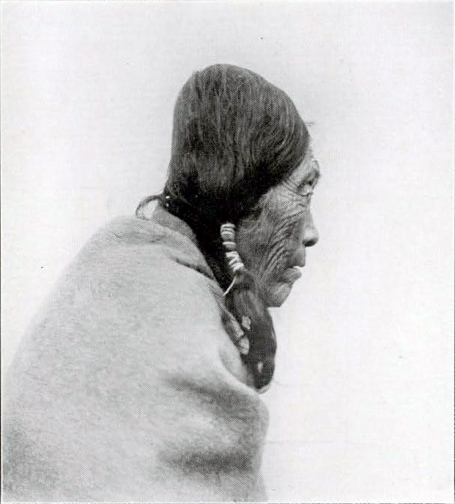 An old woman wrapped in a blanket, in profile from the chest up