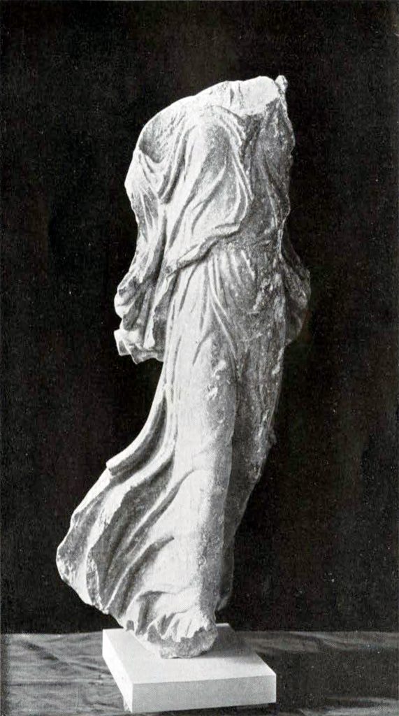 Statuette of a female goddess in flight, missing head and shoulders, draped clothing showing movement