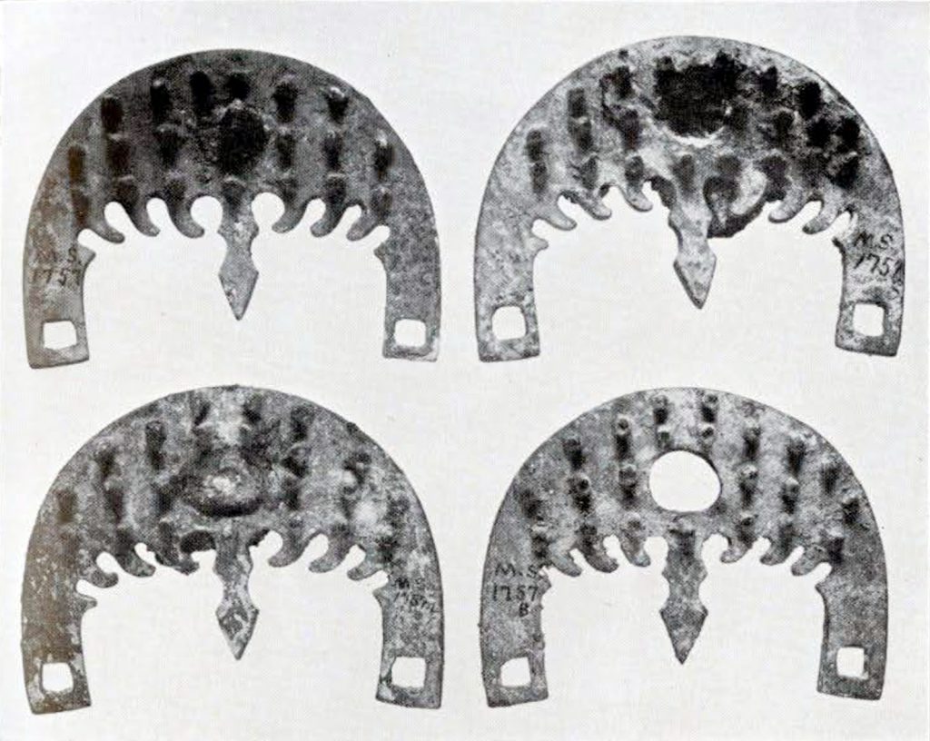 Four roughly crescent shaped bronze horse bits with many closely spaces small prongs and a square hole at each end and a circular hole in the middle