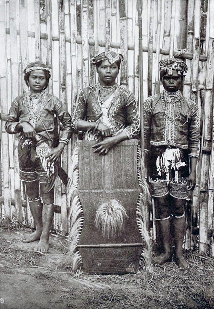Three warriors in their battle costumes, holding a large shield