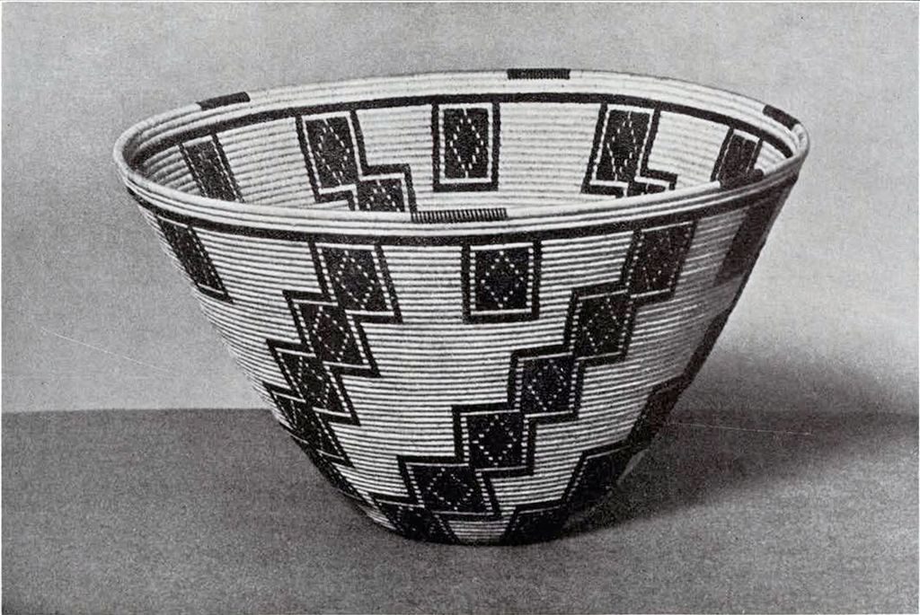A coiled, bowl shaped basket with red and black outlined stacked squares as pattern
