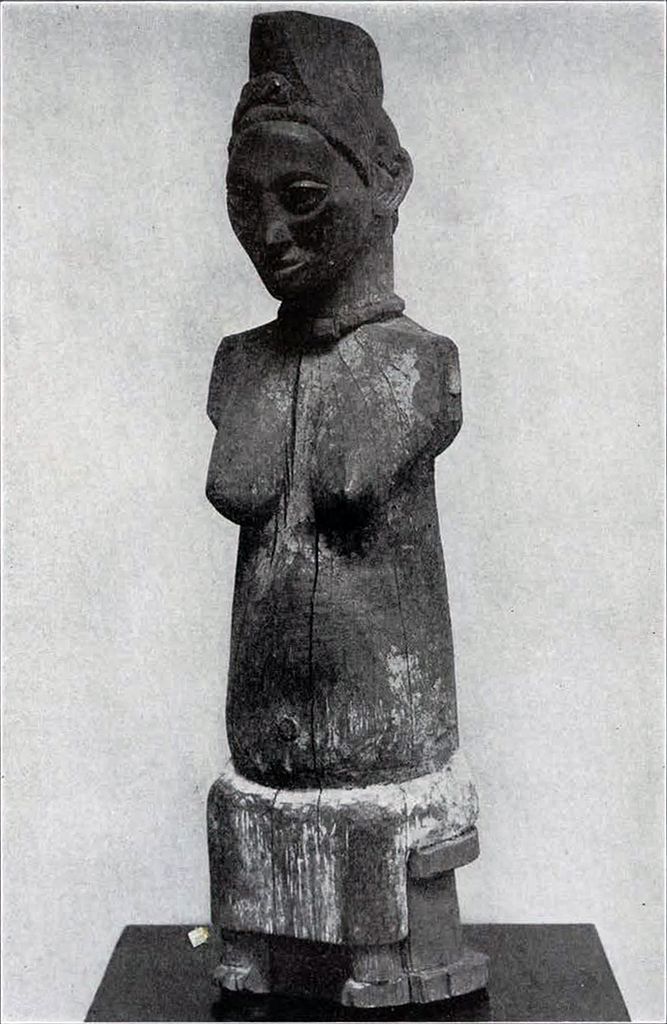A wooden statue of a seated woman with a large, crested coiffure, arms missing