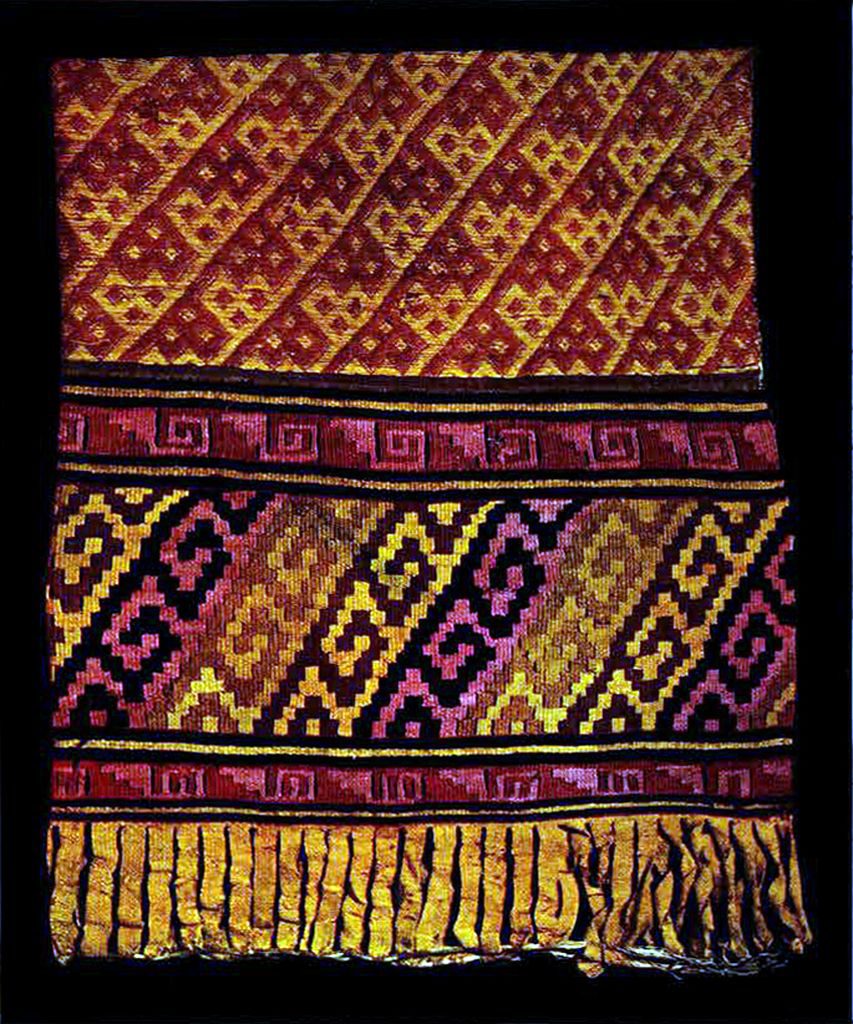 Part of a brocade garment with many colorful patterns and a fringe