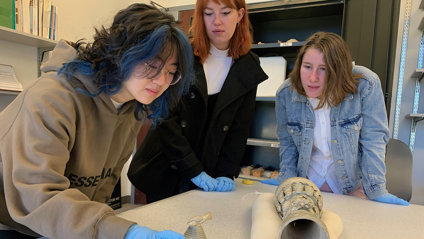 Three students examining an urn on a table.