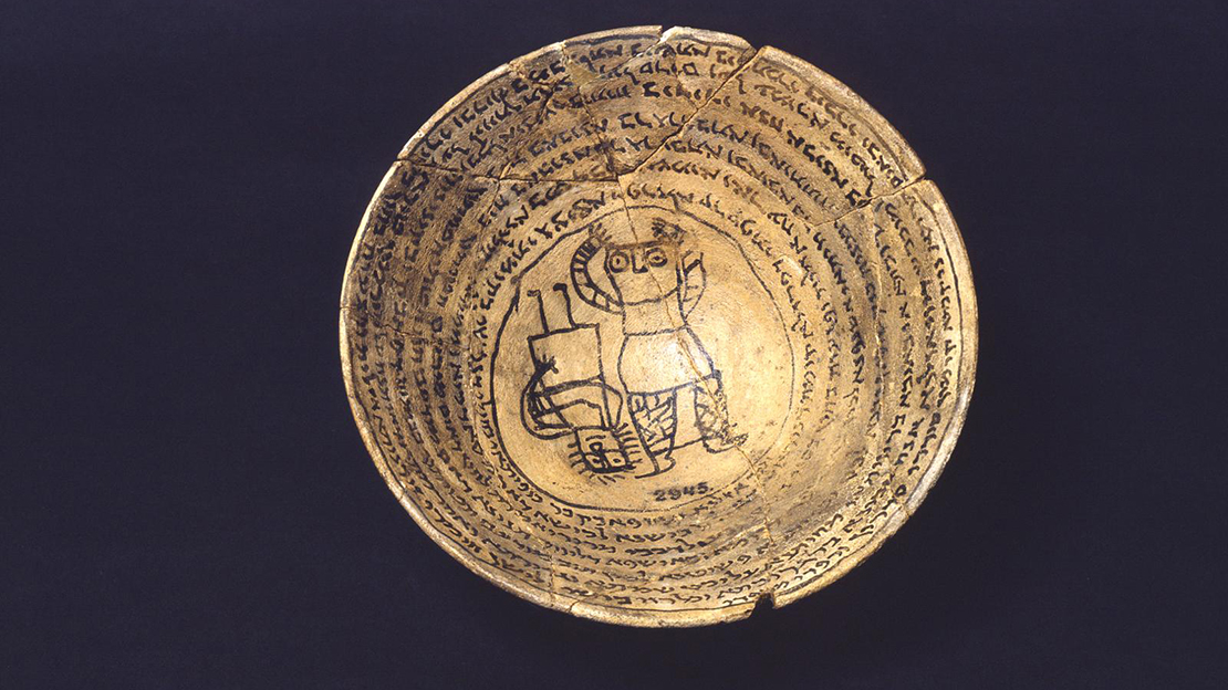 A terracotta bowl with a figure drawn at the bottom, surrounded by rings of text