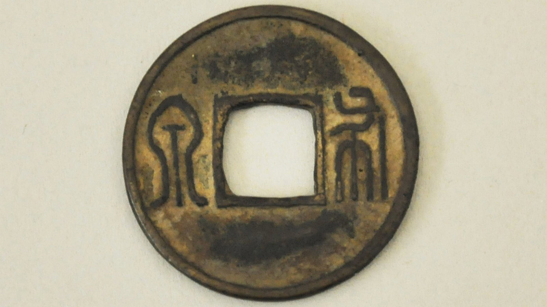 An engraved coin with a square hole in the middle.