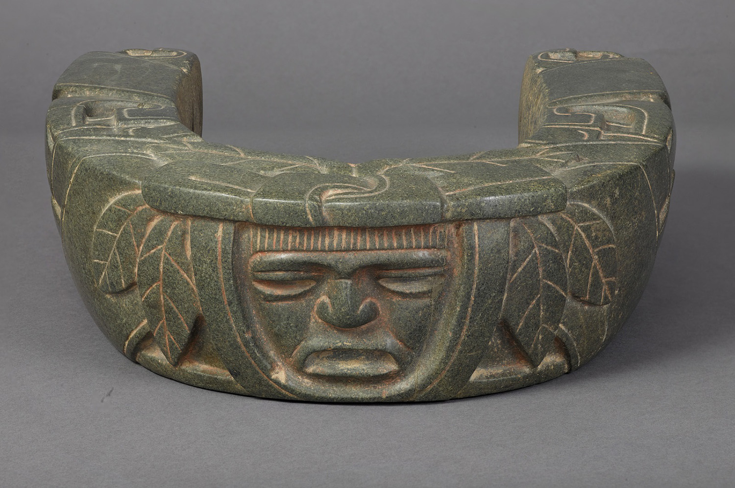 Greenstone yoke with human faces carved on it.