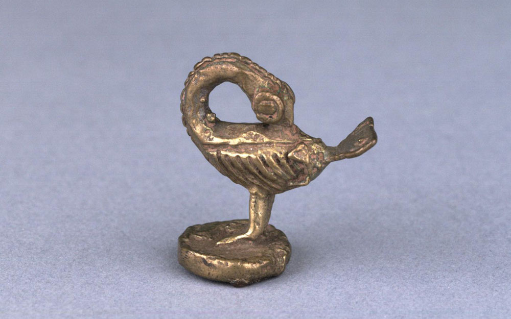 Ashanti gold weight in the shape of a bird pecking back, on round base.
