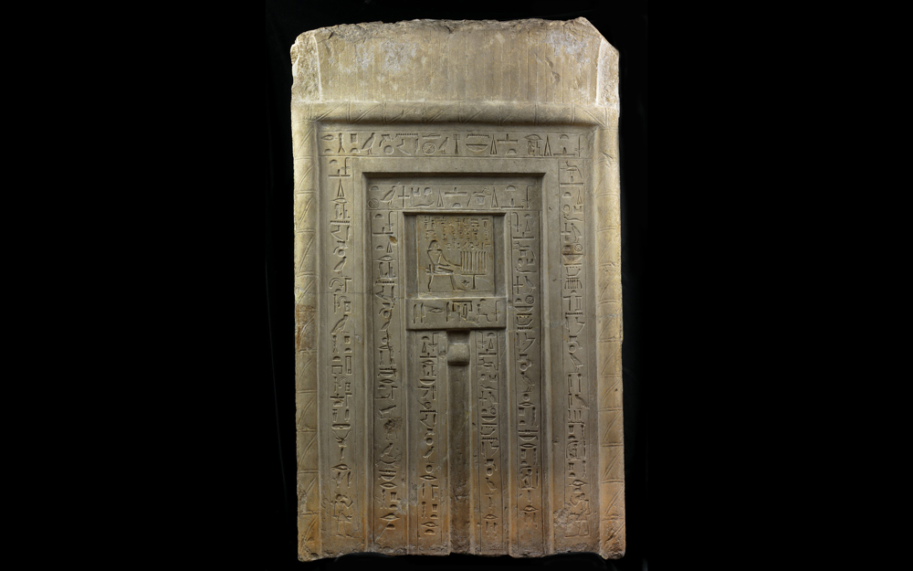 False door. On the central panel, the deceased is shown seated before a table of offerings. The text is a standard funerary inscription invoking the funerary gods Osiris and Anubis.