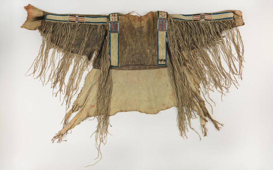 Buckskin with bands of quill work across shoulders and down sleeves, with long cut leather fringe, among which are scalp locks at sleeve.