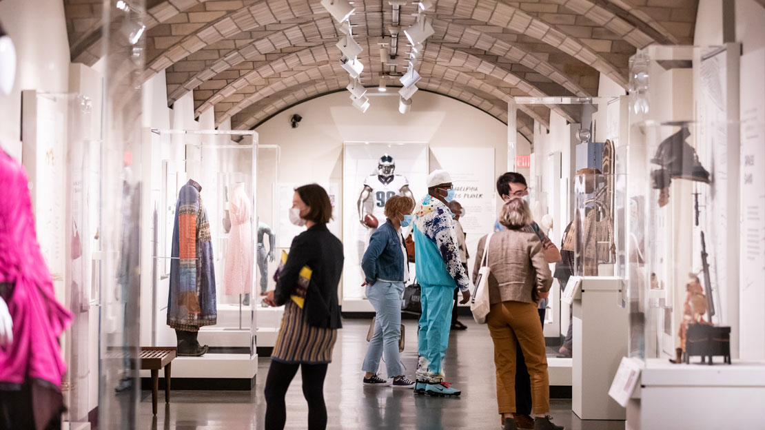 A view of the Stories We Wear exhibition, with people admiring the artifacts.