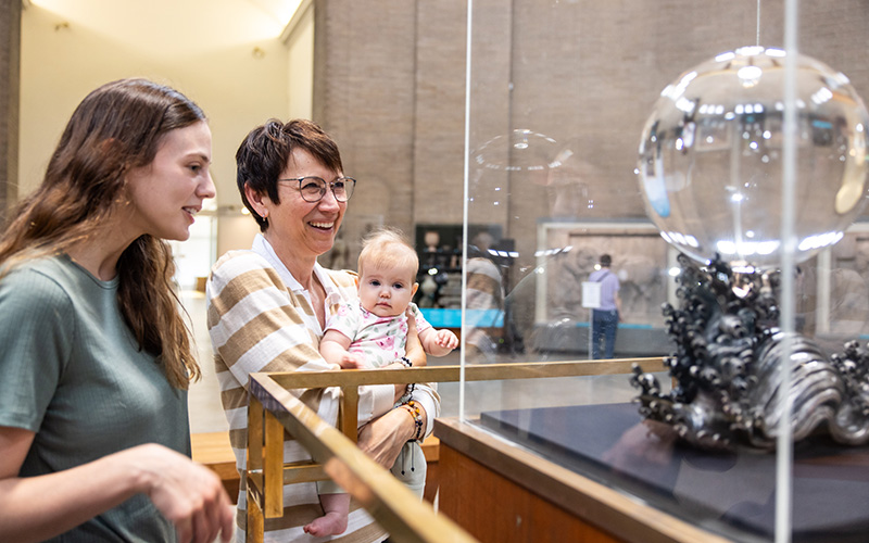 Two women and a baby looking at a glass ball on display.