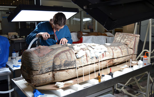A museum conservator working on a sarcophagus in a lab.