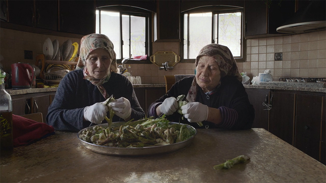 Two elderly women preparing herbs in kitchen.