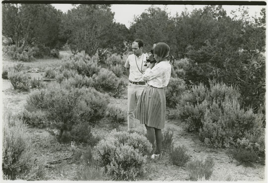 Two people in the brush, filming something with a handheld camera.
