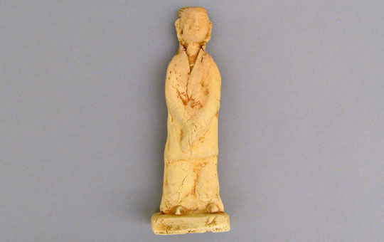 Unglazed, standing female figure dressed in tunic and trousers. More crudely made than other in the set.