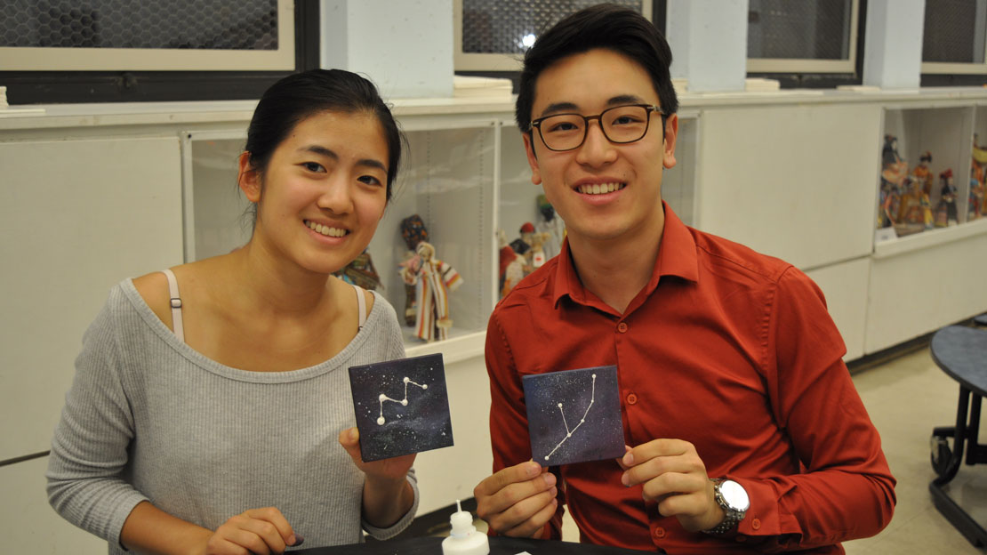 two students showing off paintings of constellations they made