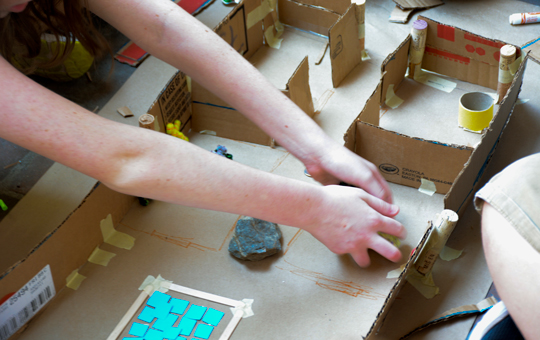 A child making a reconstruction of a home using scrap materials.