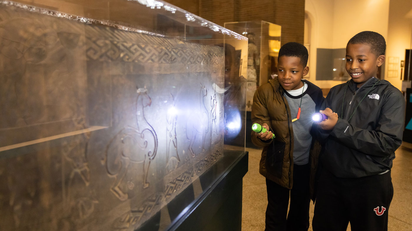 Two boys admiring an artifact using flashlights.