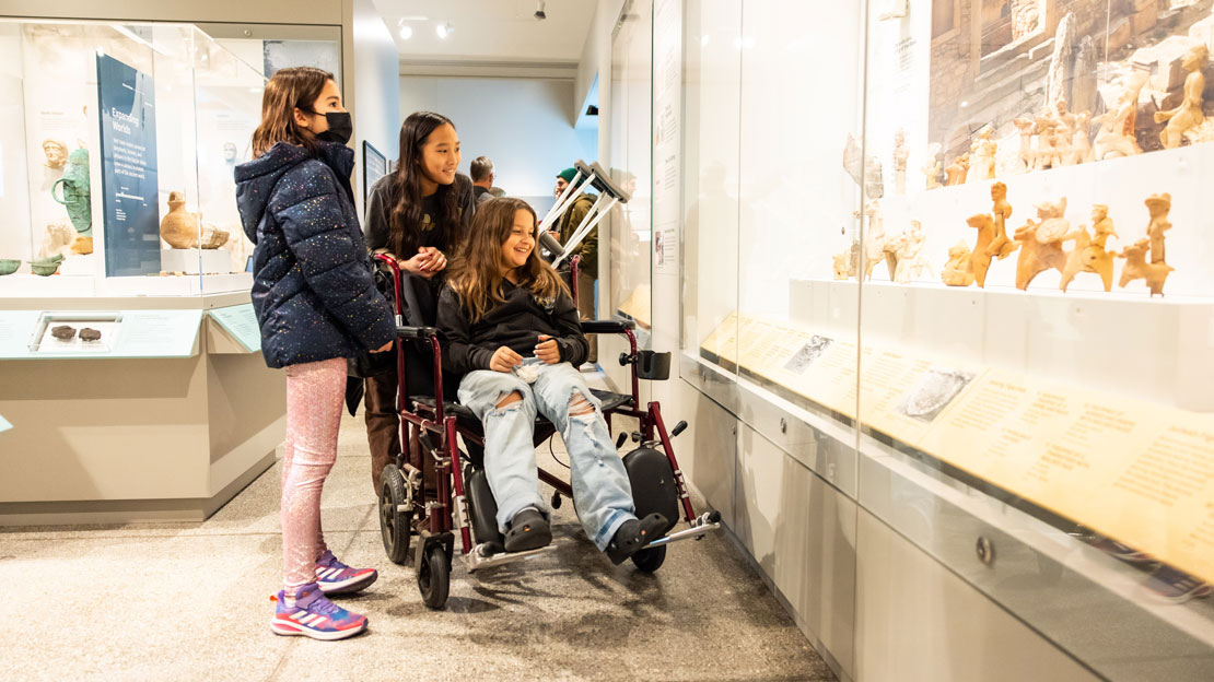 A girl in a wheelchair with two friends in a gallery.