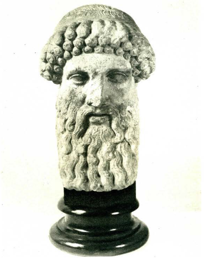 Male statue head with curly hair and a long wavy beard and moustache