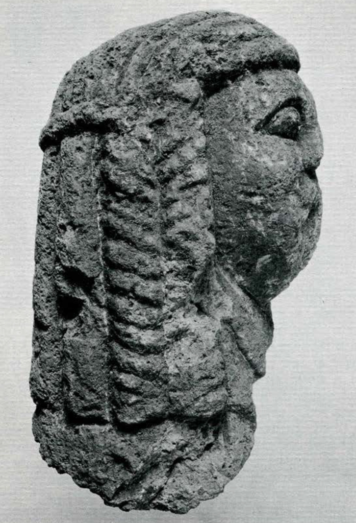 Crude carved porous stone head with braided hair