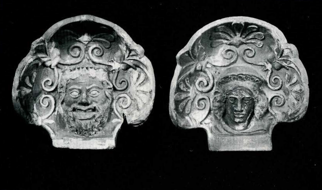 Two shell shaped antefixes with faces in the midst of organic decoration