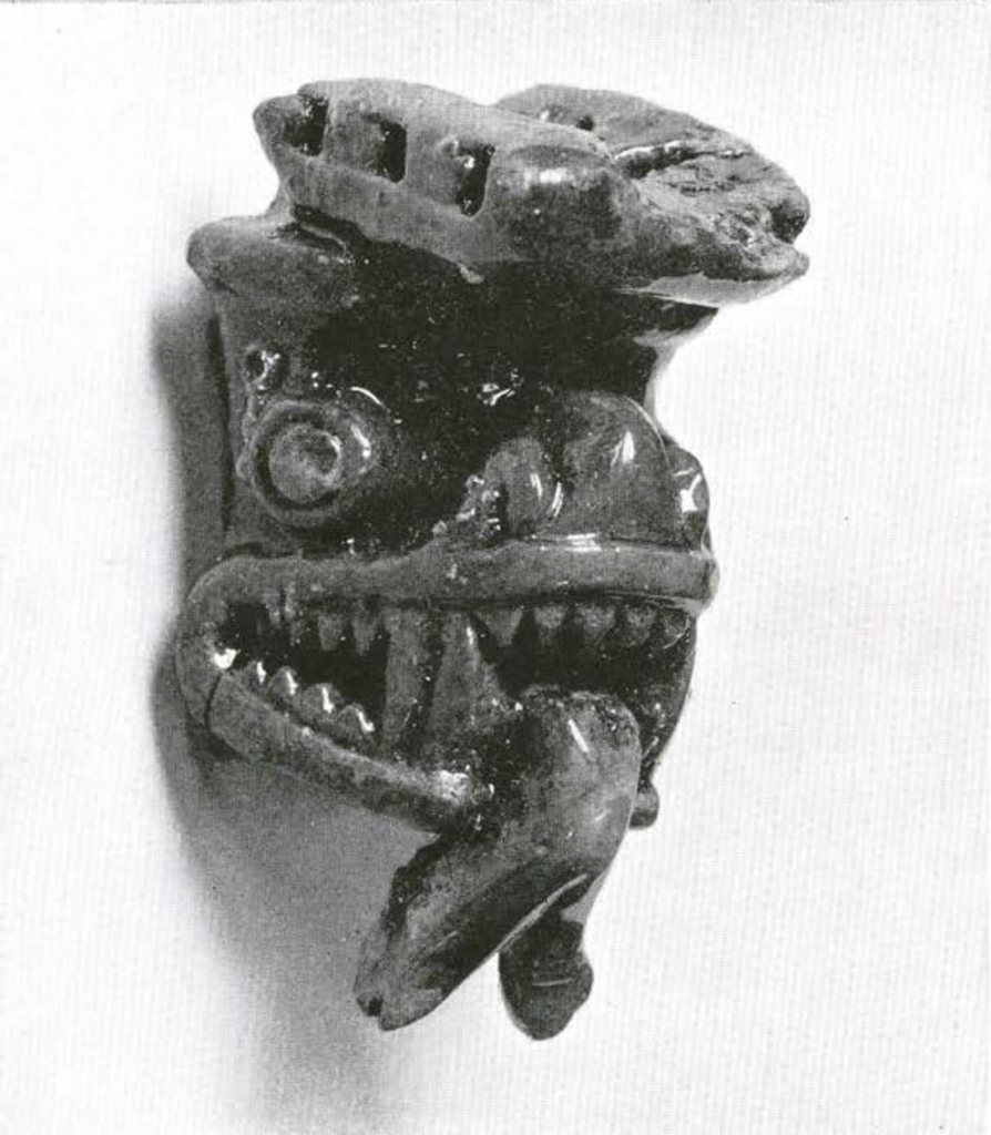 Bone carving of a face with a forked tongue and flat headdress