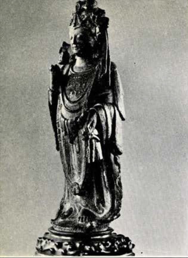 Statue of a Bodhisattva in elaborate draped clothing and jewelry, holding a flower in right hand from which has sprung a small deity