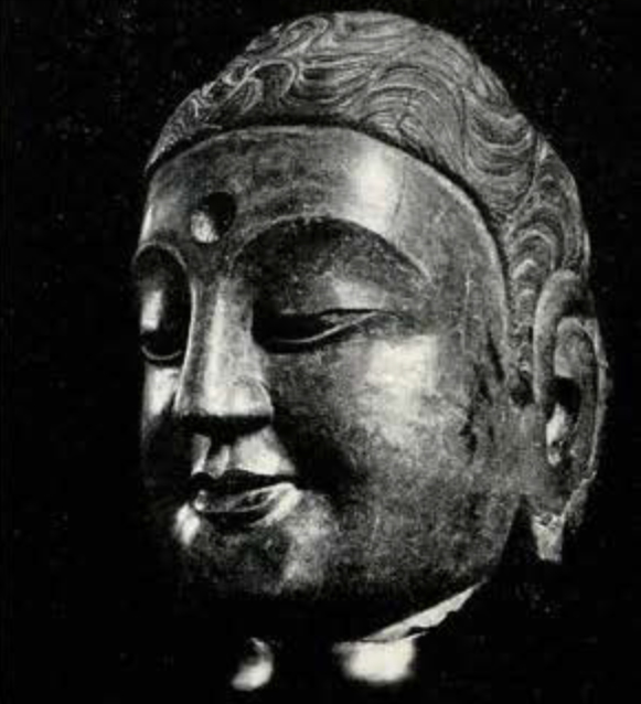 Stone head of a buddha with wavy Greco-Roman influenced hair, downturned eyes, large cheeks and long earlobes