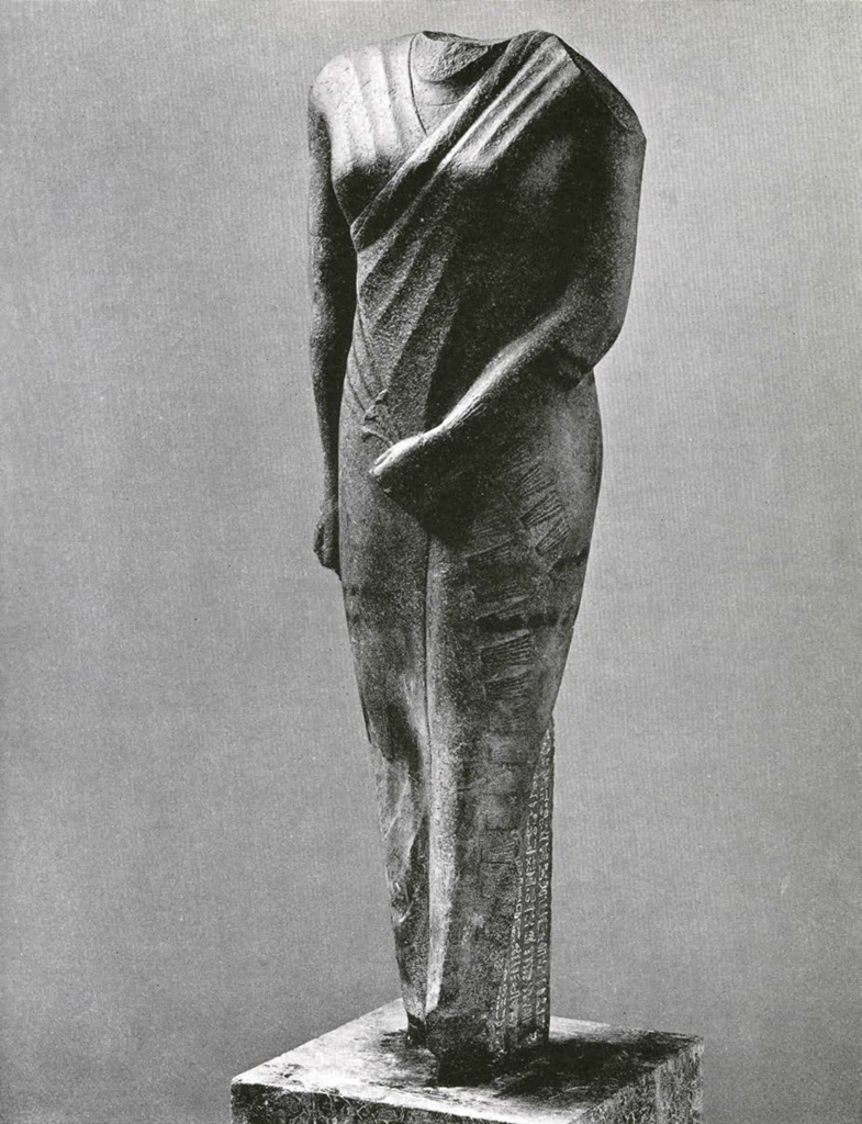 Headless statue of a man in a fitted garment with fringe, with columns of hieroglyphs
