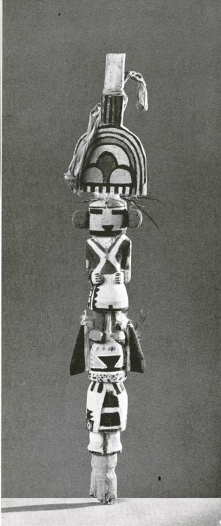 Two Katchina dolls, one standing on the shoulders of the other, topped with a rainbow headdress