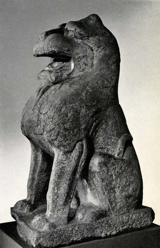 Massive carved stone seated lion with mouth open and curled inward mane in low relief